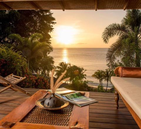 Serene balcony view of sunset over sea with tropical foliage and plush sofa.