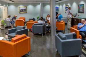 Waiting area with orange and grey chairs, people seated and standing, relaxed atmosphere.