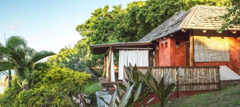 Rustic red house with wooden deck in lush tropical setting, sunny day