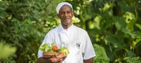 Chef in garden with basket of vegetables, promoting farm-to-table cooking.