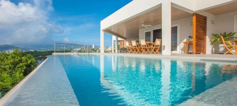 Modern infinity pool overlooking scenic hills with patio dining and lounge chairs.