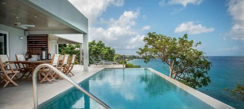 Luxurious infinity pool by the sea with dining area and panoramic ocean views