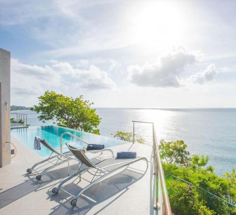 Luxurious infinity pool with sun loungers overlooking serene sea, clear sky.