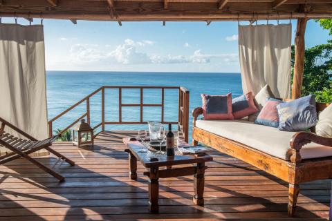Stylish outdoor lounge with sea view, plush cushions, and wine on table.