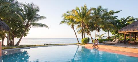 Tropical pool merging with ocean view, people relaxing at sunset
