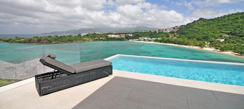 Luxury infinity pool overlooking tropical coastline with lounge chair.