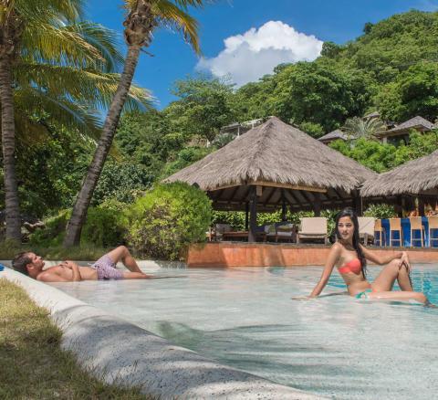 Couple relaxing at a tropical resort pool with lush greenery and palm trees