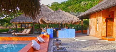 Luxurious resort pool with wooden loungers, thatched pavilions, and an outdoor bar