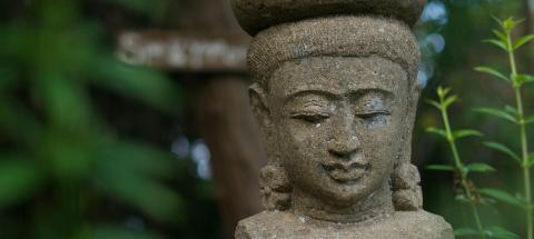 Serene Buddhist sculpture in garden setting with lush greenery.
