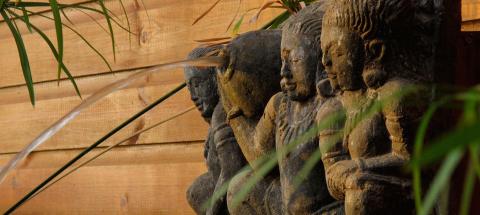 Row of ancient stone sculptures in a lush garden with a water stream.