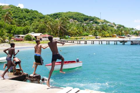 Three boys playing on a sunny dock with a boat and lush hill in the background