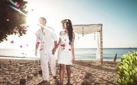 Wedding couple on beach under red petals, white canopy backdrop, sunny day
