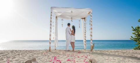 Wedding ceremony on beach with couple under decorated canopy facing ocean.