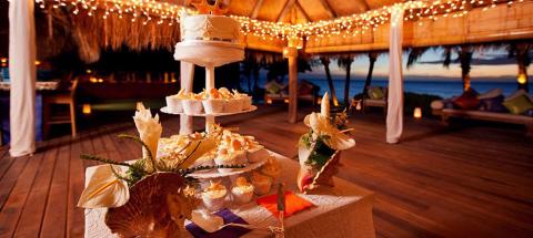 Outdoor wedding reception with cake and dessert table near the beach at twilight.