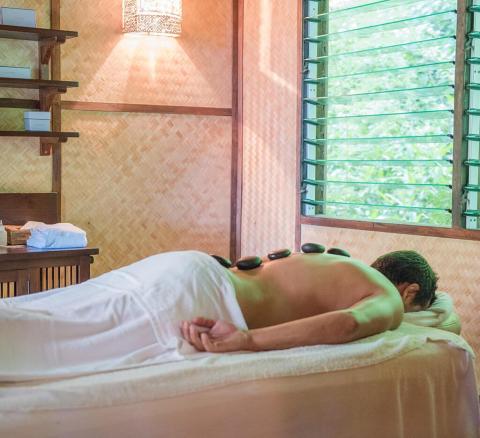 Person receiving hot stone massage in serene spa setting with greenery.