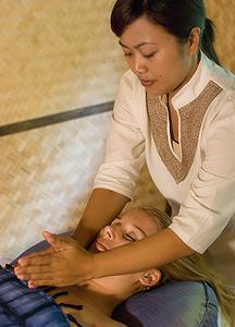 Asian practitioner giving massage in serene spa setting with bamboo mat.