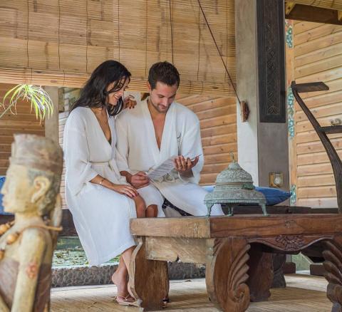 Man and woman in robes at spa reviewing a brochure, smiling.