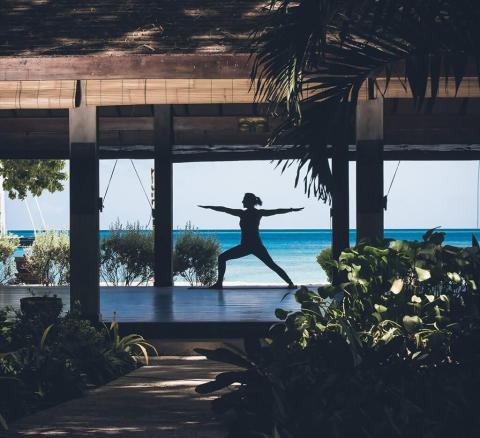Person doing yoga on a wooden platform with sea view, promoting relaxation and wellness
