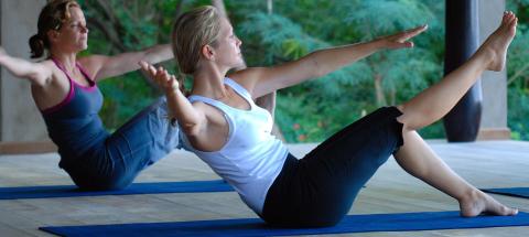 Two women practicing yoga on blue mats in a serene outdoor setting