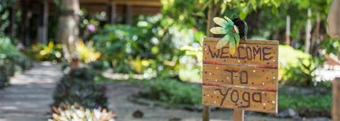 Rustic wooden Welcome to Yoga sign with green leaf detail on garden path.