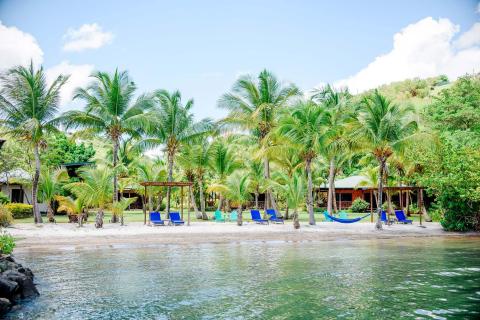 Relaxing tropical beach with chairs, hammocks, and resort cabins under clear skies.