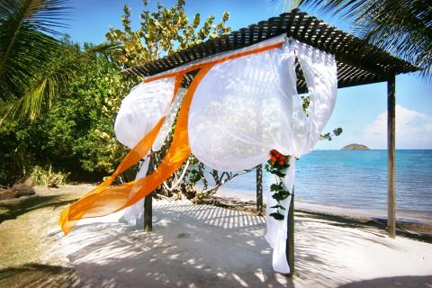 Seaside gazebo with white drapes and orange ribbons for a wedding on a tropical beach.