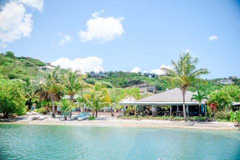 Tropical waterfront with restaurant, boats, and hills reflecting in serene waters
