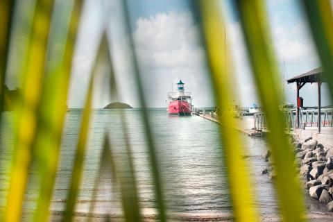 Scenic coastal view with red boat and sailboats docked at piers under cloudy sky