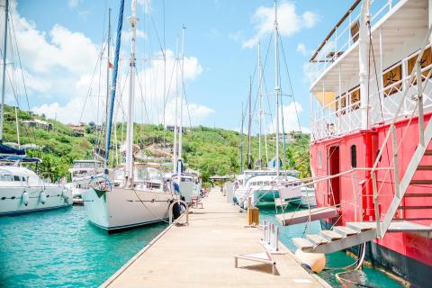 Vibrant marina view with yachts, a red houseboat, and green hills under a clear sky.