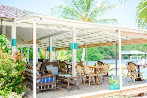 Outdoor tropical dining area with wicker chairs under a white pergola by the sea.