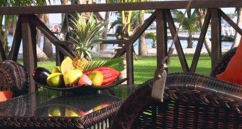 Luxurious tropical outdoor dining setup with fruit bowl by serene waterfront