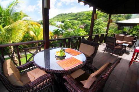 Outdoor dining on a deck with lush greenery, wicker furniture, and a fruit bowl centerpiece.