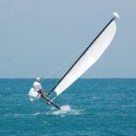 Windsurfer tilting sail on blue ocean, clear sky visible