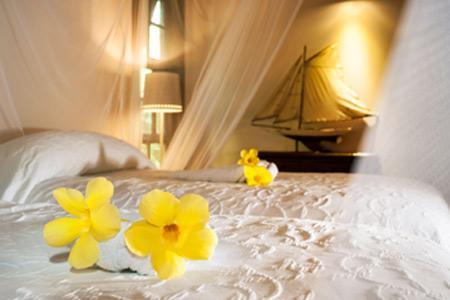 Elegant bedroom with white bedding, yellow plumeria flowers, and model sailboat decor.