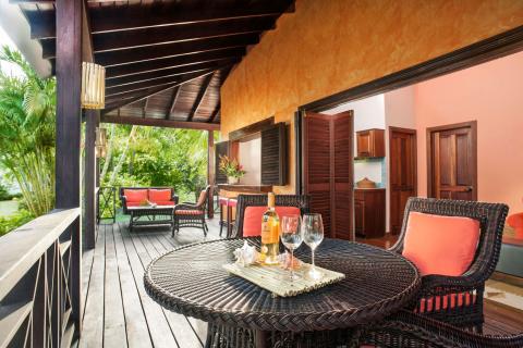 Tropical patio with wicker furniture, wine, and cushions, ideal for relaxation and entertainment.