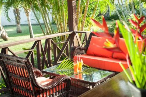 Tropical patio with wicker furniture, red cushions, and lush greenery in a sunny setting