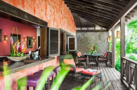 Stylish outdoor lounge with bar, vivid stools, and lush greenery for a tropical vibe.