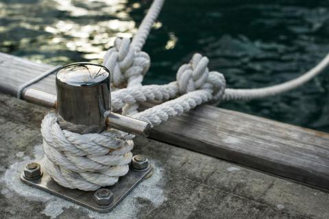Metal bollard with white mooring rope on dock, greenish water backdrop