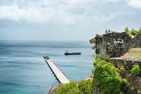 Historic ruins and pier with boat on calm sea under partly cloudy skies