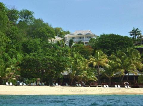 Tropical beach with chairs, palm trees, and luxury hilltop buildings overlooking the ocean