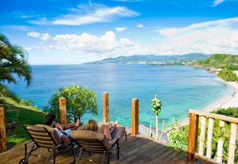 Two people relaxing on lounge chairs enjoying a scenic beach view from a deck.