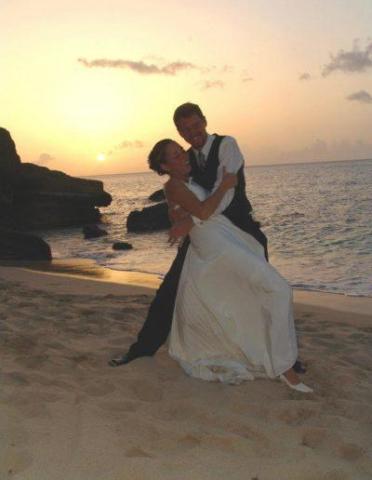 Newlyweds embracing at sunset on a beach, ocean and rocks in background