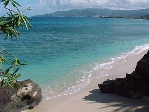 Scenic beach with clear blue-green waters, sandy shores, and distant mountains