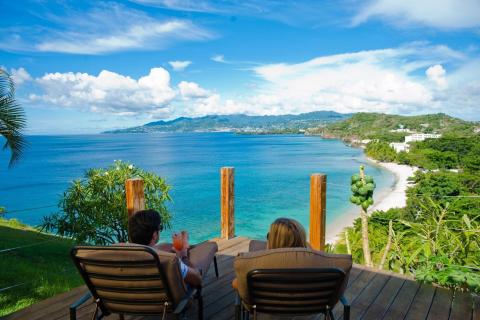 Coastal view from deck with couple enjoying drinks, serene sea and hills.