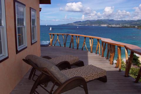 Seaside deck with ocean view, lounge chairs, and natural wooden balustrade on clear day.