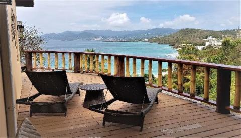 Tropical seaside view from deck with wicker chairs overlooking lush hills and turquoise sea