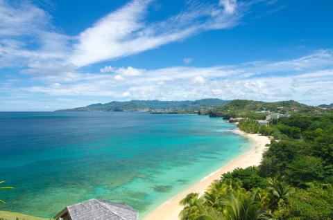 Stunning coastal view with clear blue sky, turquoise sea, sandy beach, and lush greenery.