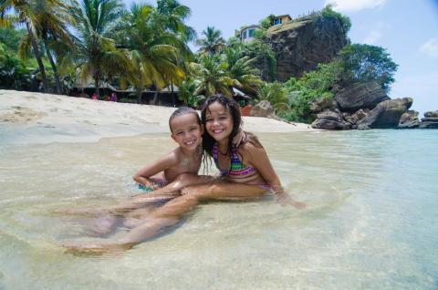 Joyful children playing in shallow water at a tropical beach with cliffs.