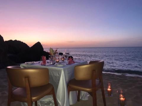 Romantic beach dinner setup at sunset with wine, facing the ocean.