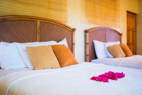 Hotel bedroom with white and orange pillows, pink rose petals on bed